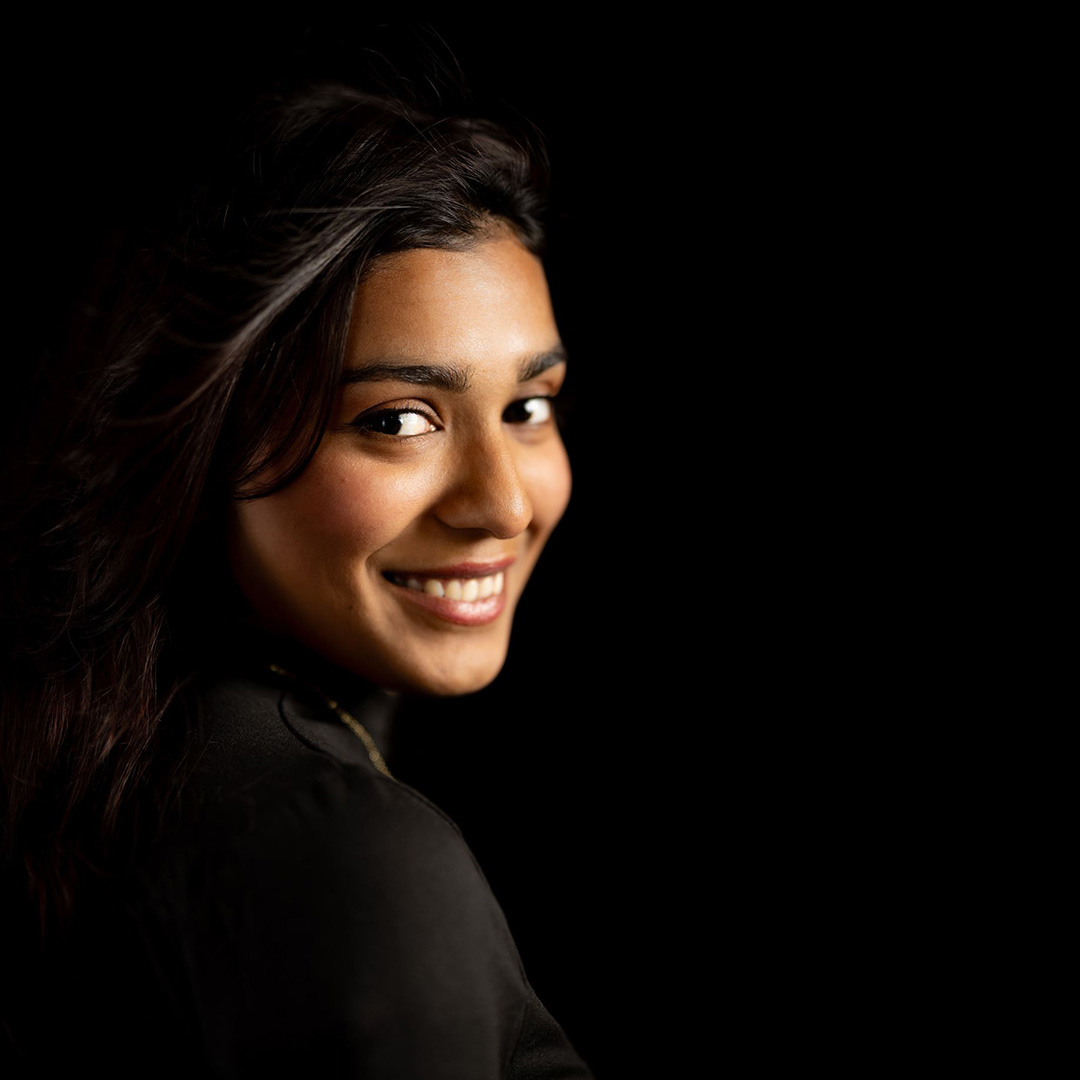 Nysa - Uxbridge College Aviation, Travel and Tourism student - smiling over her shoulder. She is wearing a black top and has long dark hair.