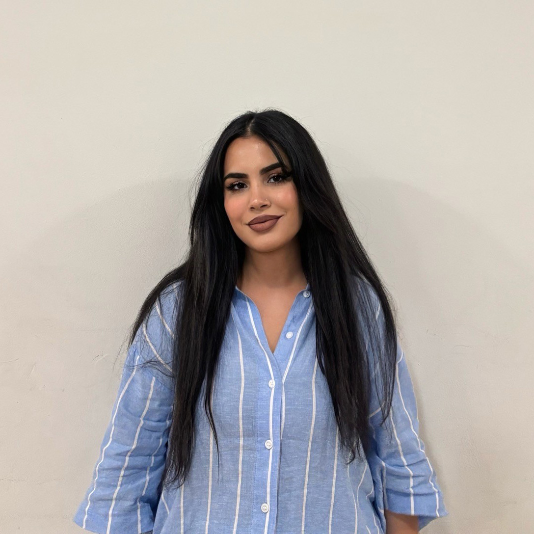 Rukhsar - she has long dark hair and is waring a blue shirt with white stripes 