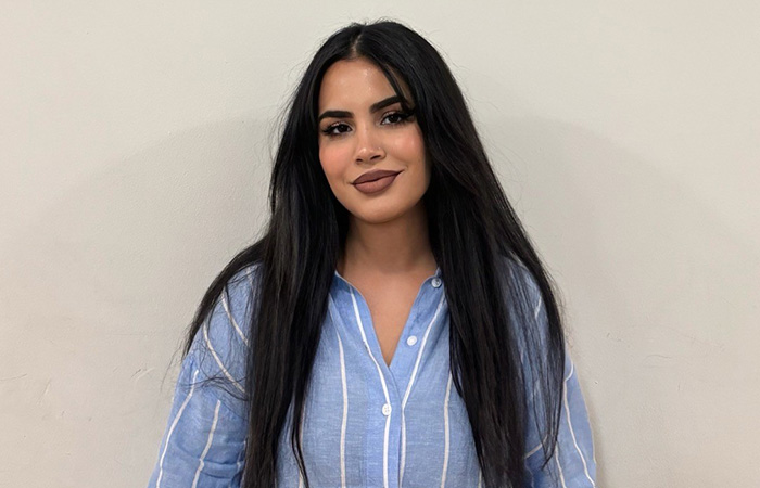 Rukhsar - she has long dark hair and is waring a blue shirt with white stripes 