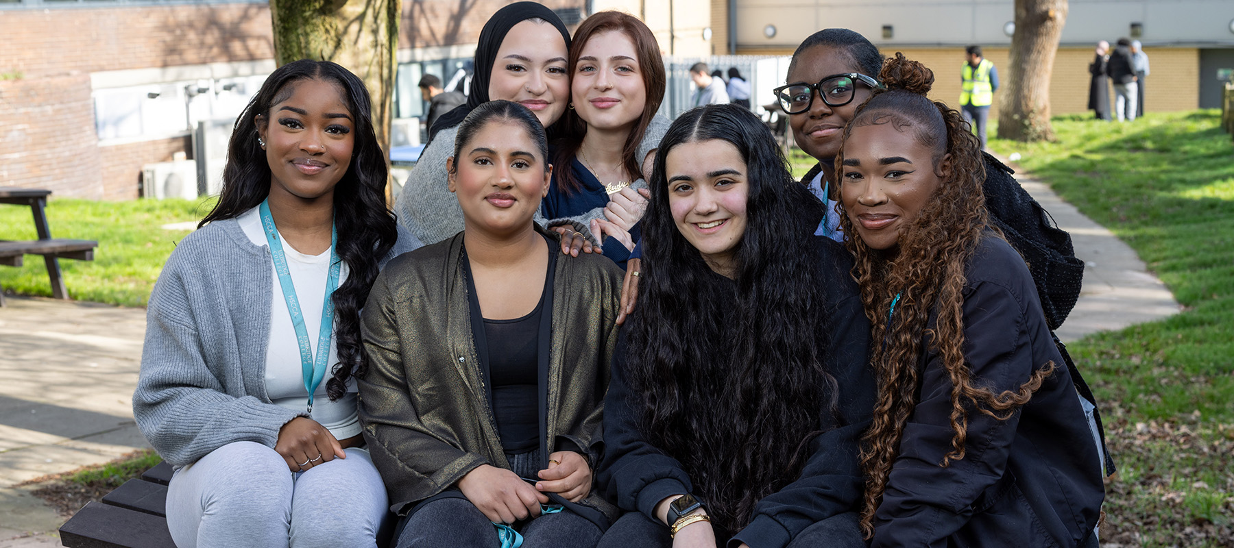 A group of female Uxbridge College students sitting together in a group on one of the tables in the outside courtyard. 