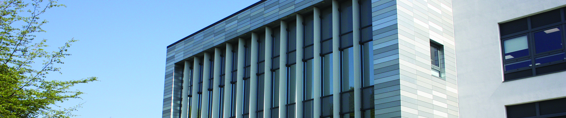 Exterior view of a building at Uxbridge College. There is a tree to the left and multiple windows in the grey building.  