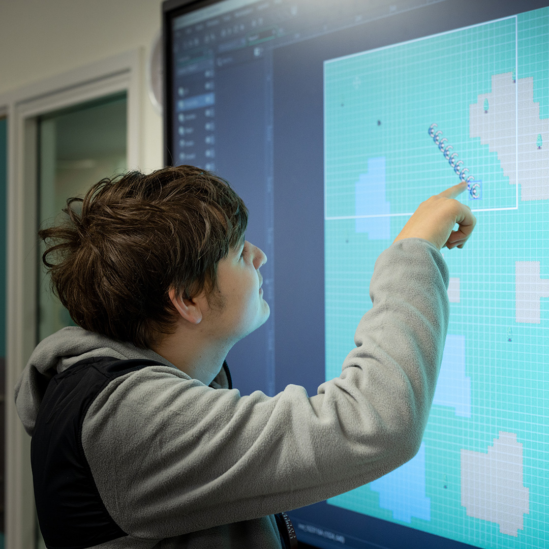 A male Uxbridge College computing student working out something on the big screen in class - he has his finger on the screen.