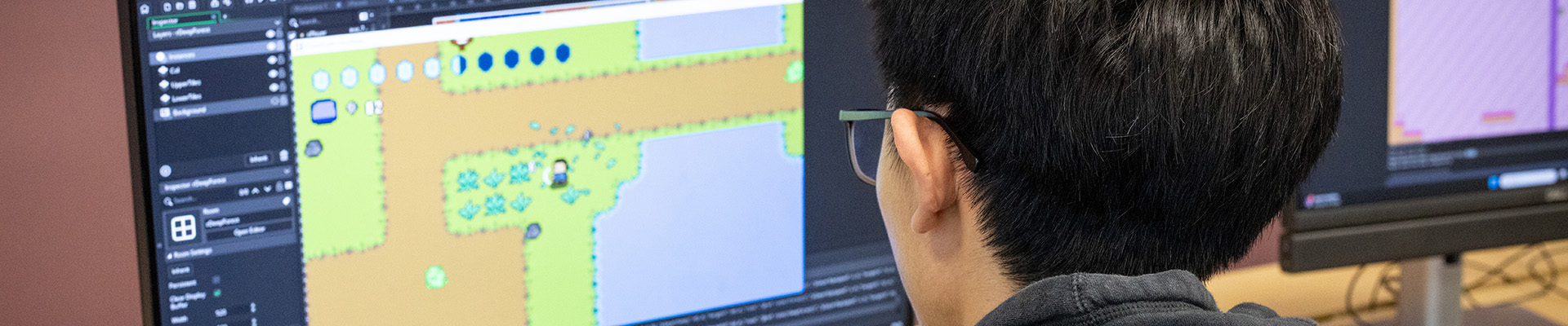 A male Uxbridge College computing games development student working on a games project. He is looking at a computer screen and there is a picture of a game on there.