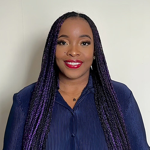 Natasha is smiling and wearing a purple/blue shirt with long purple braids.