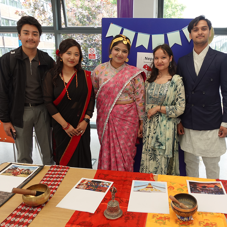 Uxbridge studetns at one of the Culture Days 2025, some wearing their traditional cultural dress. Four people are standing in front of thier stand.      