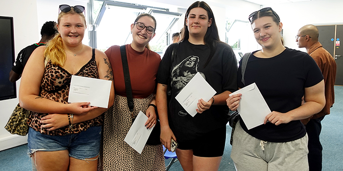 A group of four female Uxbridge students holding their letters with their A-Level results and smiling at the camera.        