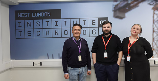 Sam Al-Jajjoka, Section Manager for Computing & IT with former Cyber Security students Danny O'Leary and Karla Gespaher. Standing in front of a West London IoT sign.