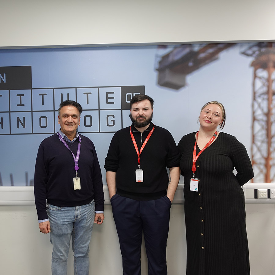 Sam Al-Jajjoka, Section Manager for Computing & IT with former Cyber Security students Danny O'Leary and Karla Gespaher. Standing in front of a West London IoT sign.