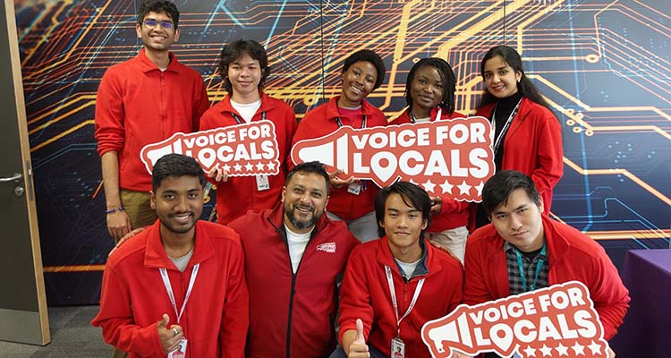 Students from Harrow, Richmond and Uxbridge Colleges (HRUC) posing for a group photo holding Voice For Locals (VFL) signs. They are all dressed in red jackets.