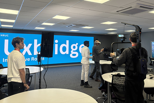 Meet the Principal Video behind the scenes footage - Clive is wearing VR headset in the Uxbridge immersive room with a film crew around him.