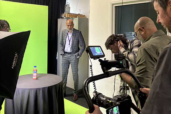Meet the Principal Video behind the scenes footage - Clive is standing next to a green screen with a media crew in front of him.