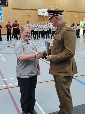 A female Uxbridge College Uniformed Services student receiving an award from Major Tom Hallett from the London District Youth Engagement Team, Army Reserve. Major Hallett is wearing his uniform, shaking the student's hand and holding the trophy.