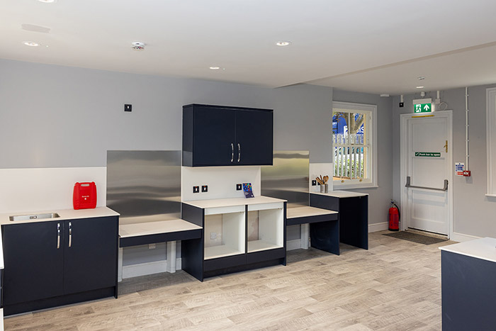 Barra Hall kitchen area - dark blue cupboards and white bench tops with windows to the right - a light and bright space.