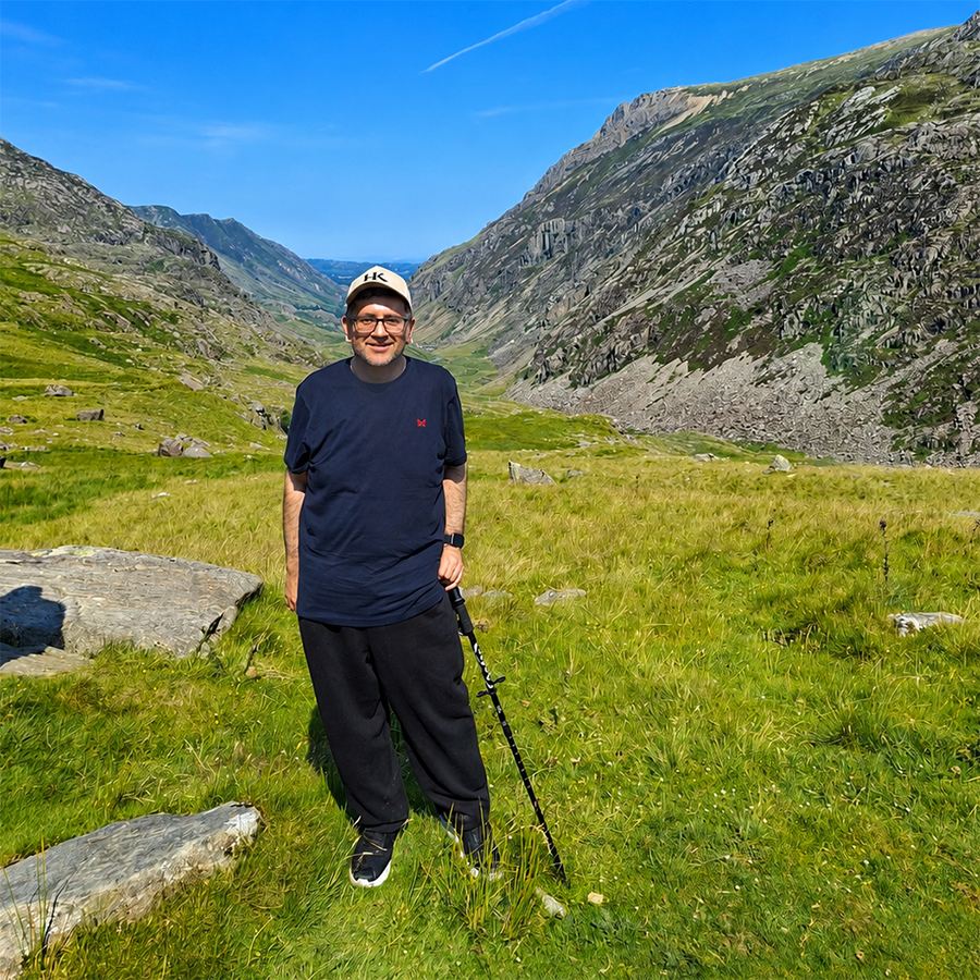 Asif Khan - Assistant Principal for Engineering, Technologies, Higher Education - on his epic walking challenge. He has green grass, rocks and mountains around him with clear blue skies. 