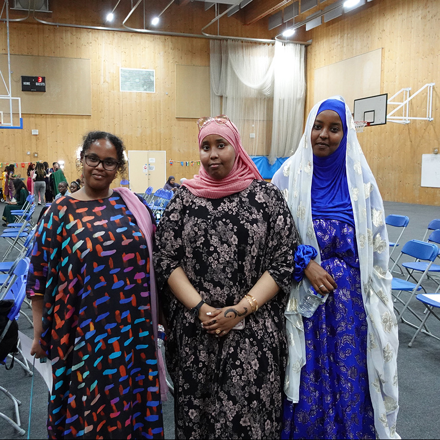Three Female Uxbridge College students dressed to celebrate the Celebration Day Cultural Event in their own cultural dress. They are wearing colourful dresses and standing in the Sports Hall.    