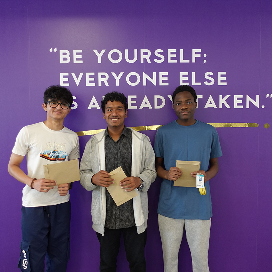 Three male Uxbridge College students holding their GCSE exam results envelopes and standing in front of a purple wall with the quote from Oscar Wilde that says: Be yourself; everyone else is already taken.           