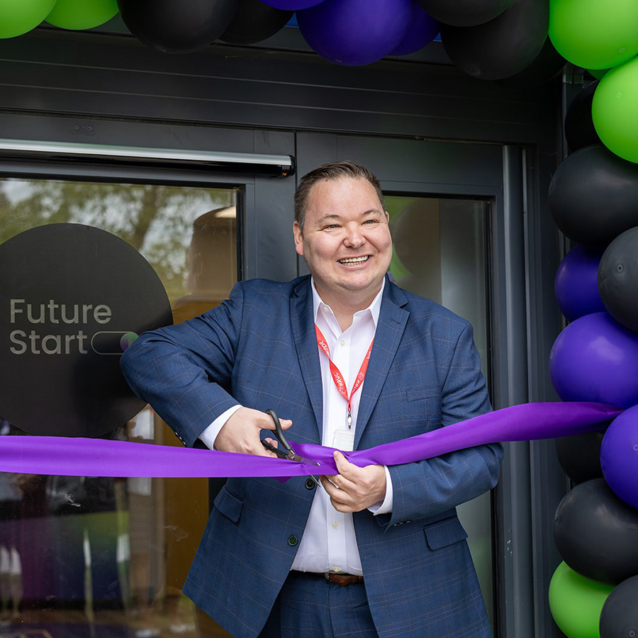 Andrew Western MP, Minister for Employment cutting the purple ribbon at the new Future Start youth employment hub. There are black, green and blue balloons behind him with a window with the Future Start logo.