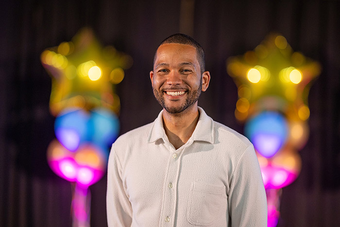 Anthony Bennett - guest speaker at the Uxbridge College Student Awards ceremony. He has gold star balloons and other balloons blurred out behind him.