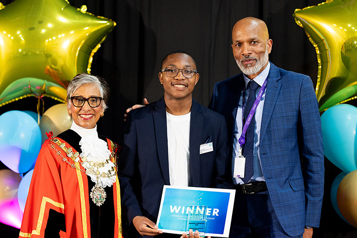Clive Hodge, Principal of Uxbridge College, The Worshipful Mayor of the London Borough of Hillingdon, Councillor Reeta Chamdal and Level 3 Health and Social Care student Nigel Nkomo holding his Principal’s Award. Balloons and gold star balloons are at the back of them. The Mayor is wearing her ceremonial robes.