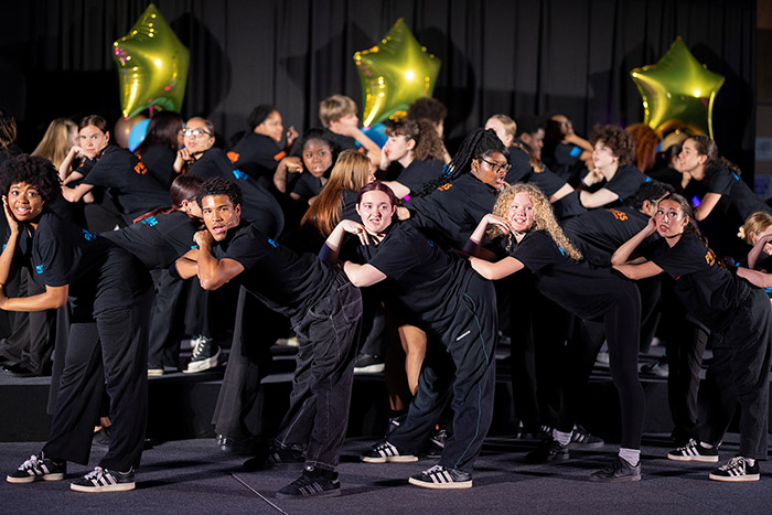 Uxbridge Colleg's Praxis Performing Arts students showcasing their skills and dancing on stage at the Student Awards ceremony. They are all wearing black with gold star ballons behind them.