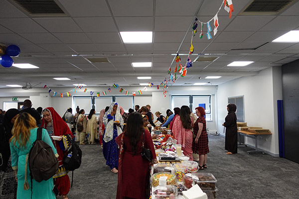 Students and staff enjoying an international lunch as part of the Celebration Day Cultural Event. There are flags hanging from the ceiling and long benches of food.